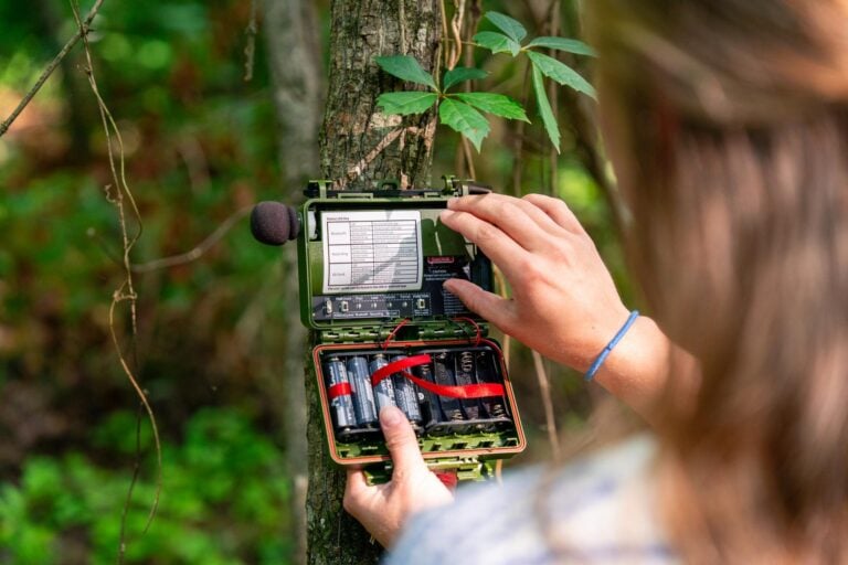 A young woman facing away from the viewer adjusts the electronic interface of a recording device.