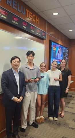 An Asian American man, a man of Asian descent, and three white women stand in a business analytics lab. They hold tiny cars.