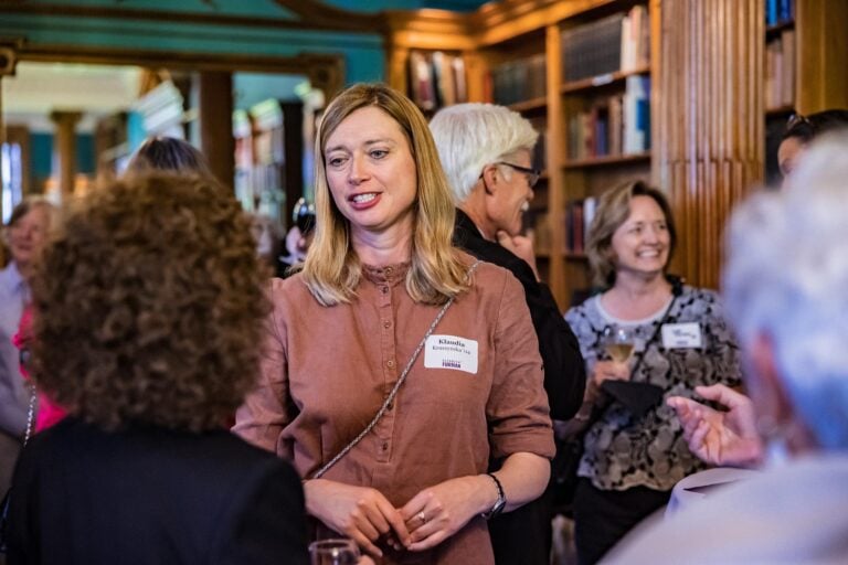 A group of adults network and talk over drinks in an indoor library.