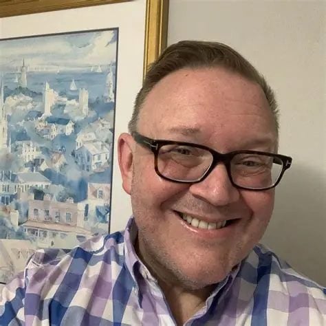 A white man wears glasses and a checked shirt in an indoor photo. Randall David Cook