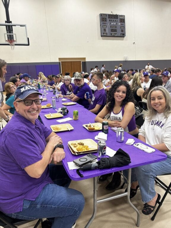 Family Weekend guests share a meal at a purple-covered table inside Furman’s Physical Activities Center.