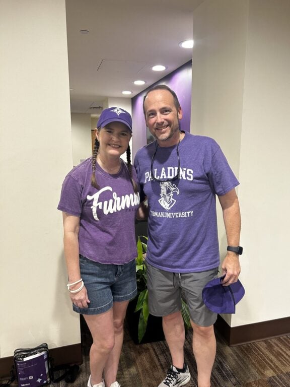 Two Family Weekend guests wearing purple Furman and Paladins shirts pose together on campus.