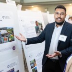 Joel Mason '25 explains details of his internship at Furman Engaged 2024. A Black man in a suit explains information on a poster to a woman.