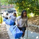 Members of the Furman football team help carry bags into Manly Hall during move-in day on Thursday, August 22, 2024. Photo by Nathan Gray, Furman University Male students carry large blue bags up stairs.