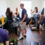 Families help new students move into a dorm room in Lakeview Hall on Thursday, August 22, 2024. Photo by Nathan Gray, Furman University Multiple students and parents unload items in a residence hall room.