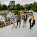 Students stroll Liberty Bridge at Falls Park in 2019. Tell-tale cranes hint of things to come.