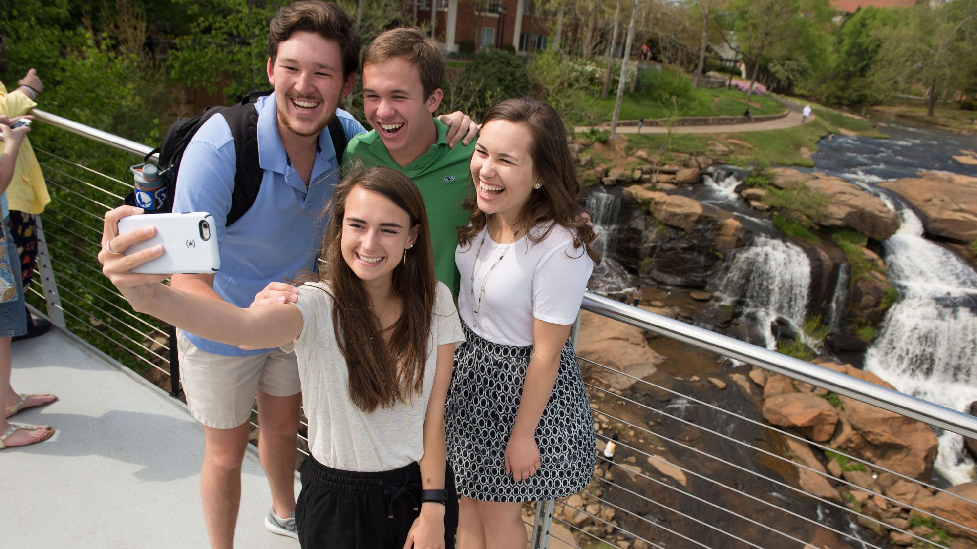 students taking photo in front of reedy river while suspended on a bridge