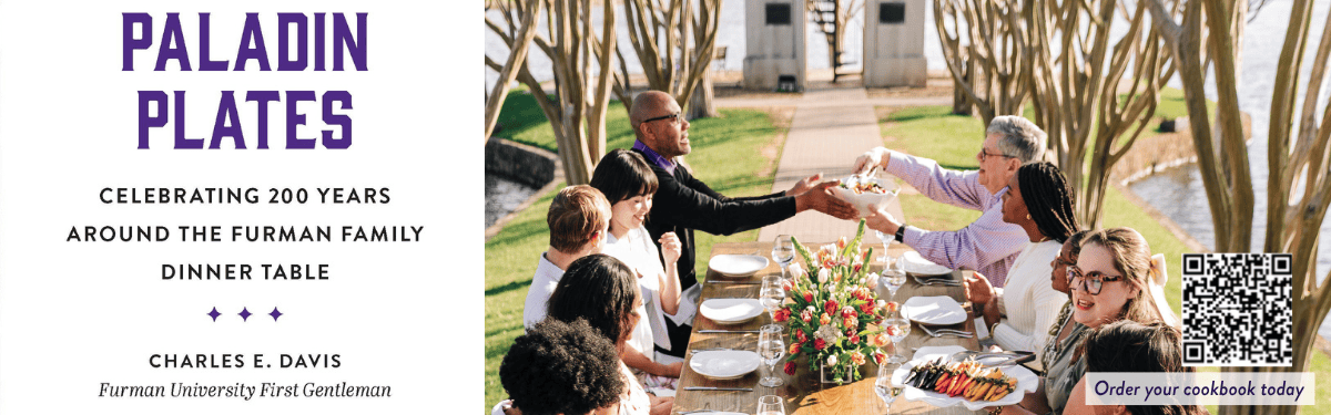 photo of a group of people gathered around a dinner table along the walkway to Furman's bell tower.