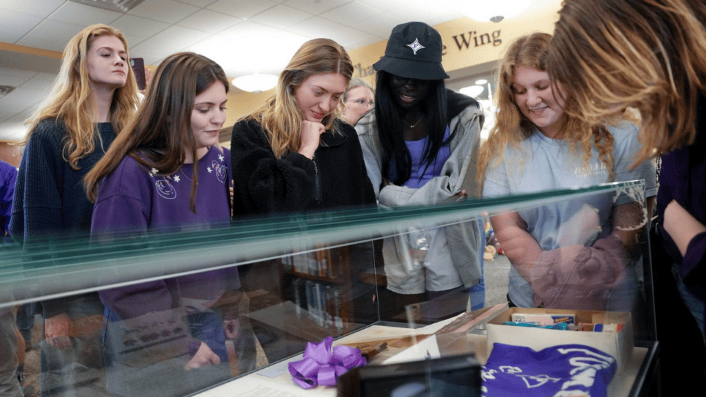 a group of students stands around a glass case, peering in. Inside the case are mementos and items saved by the Furman Class of 1993 as a time capsule project.