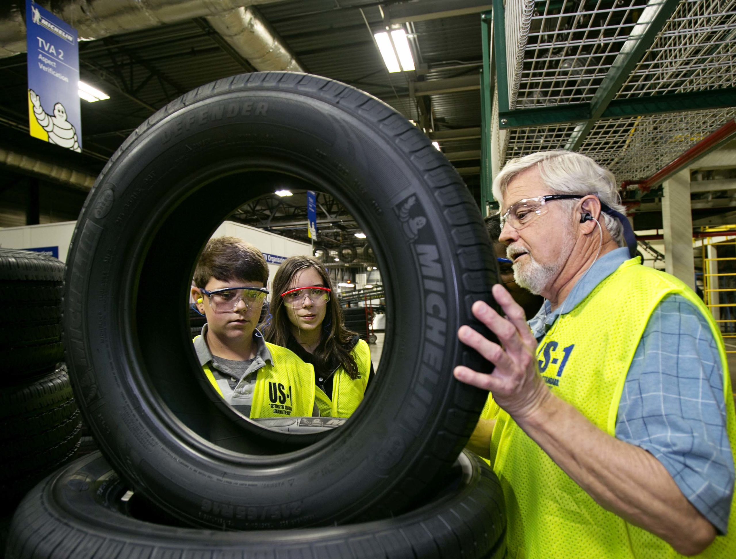 A Michelin employee showing two children a tire in a factory