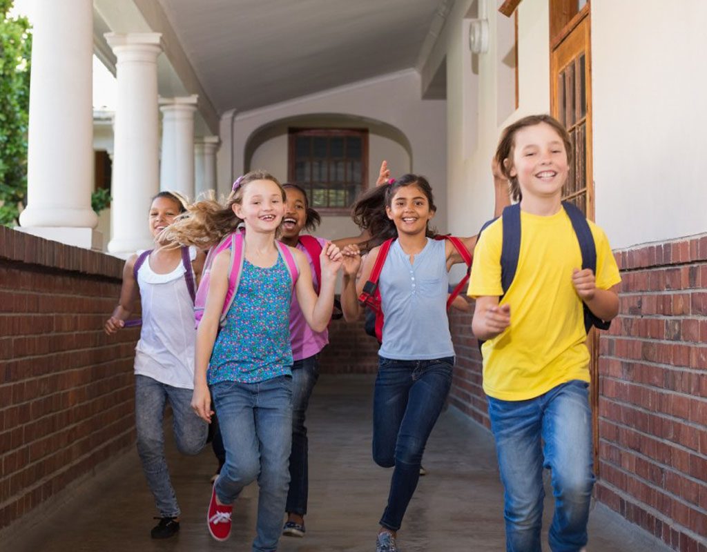 Group of children run down an outdoor hallway at school