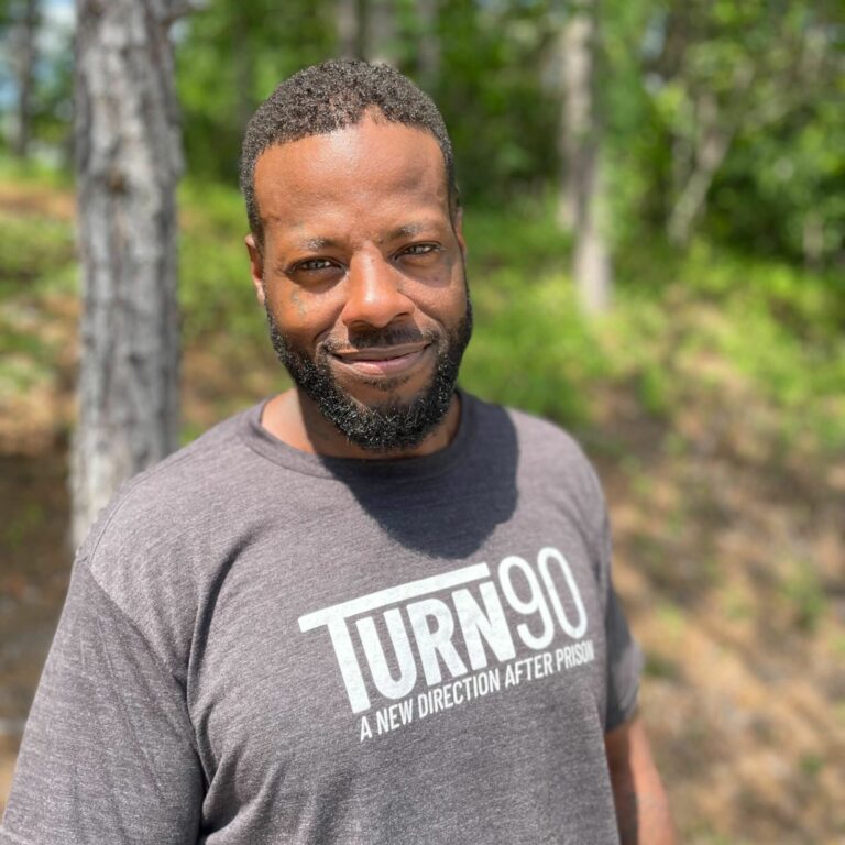 Headshot of Malik ElAmin outside in front of trees, smiling