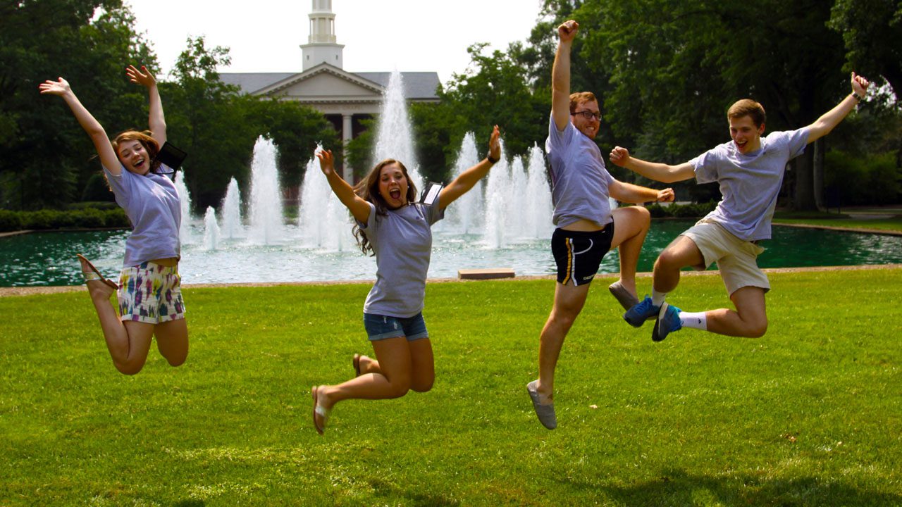 Student counselors jump in front of a fountain on a sunny day