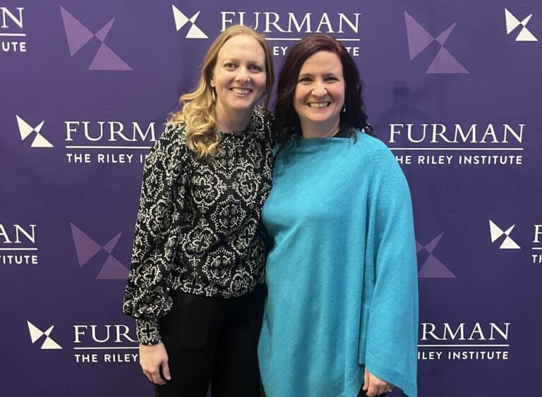 Two woman posing in front of Riley background