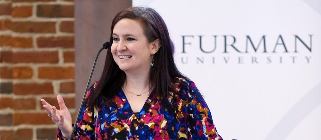 Woman in a colored shirt addresses the crowd at Graduating Scholars Reception 2026