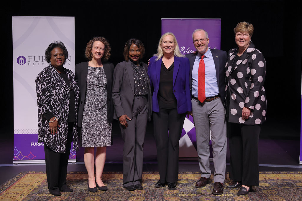 Speakers posing in front of Furman and Riley banners