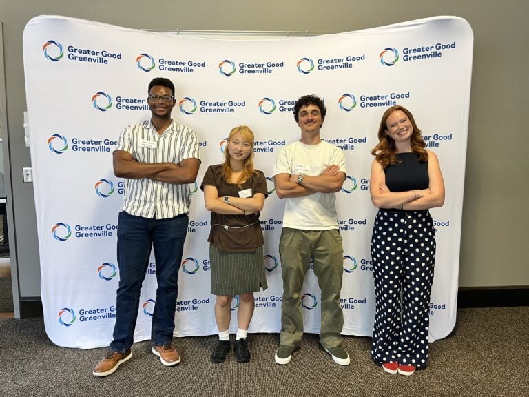 Four students stand in front of white banner