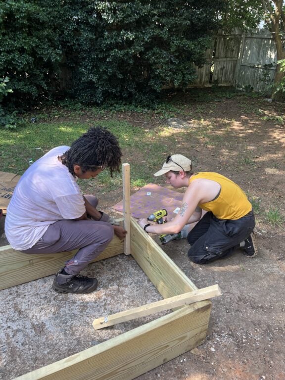 Two women attach boards for raised garden bed.