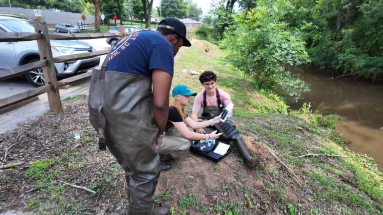 Three students conducting scientific tests on river bank