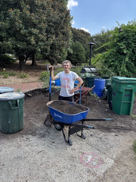 Student stands with wheelbarrow of compost