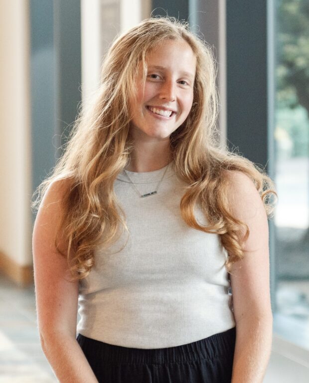 caucasian female, long blond hair, white shirt, smiling, in a bright building