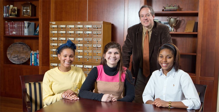 Three Furman students with professor in the library