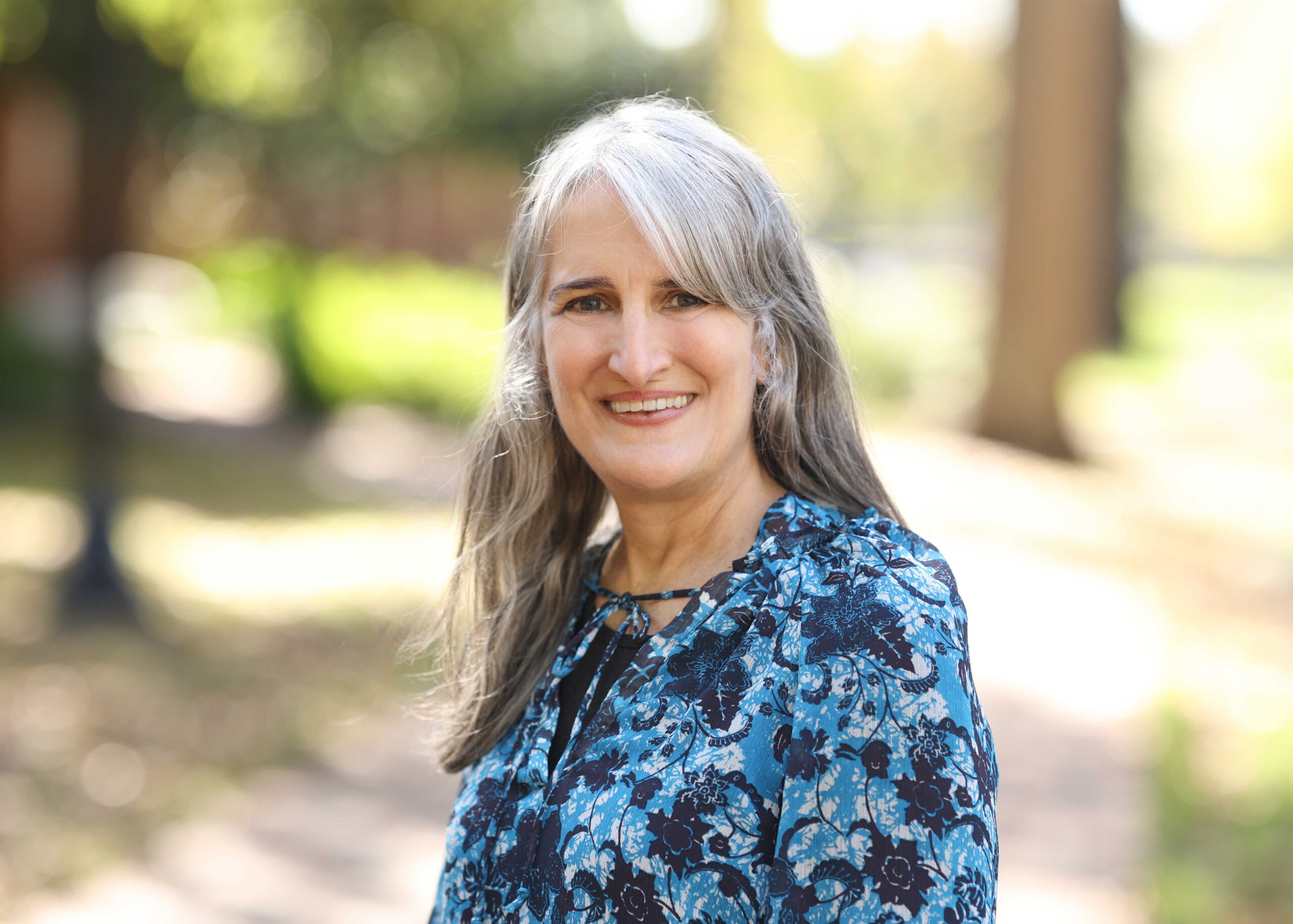 A woman in a blue shirt smiling and standing in nature