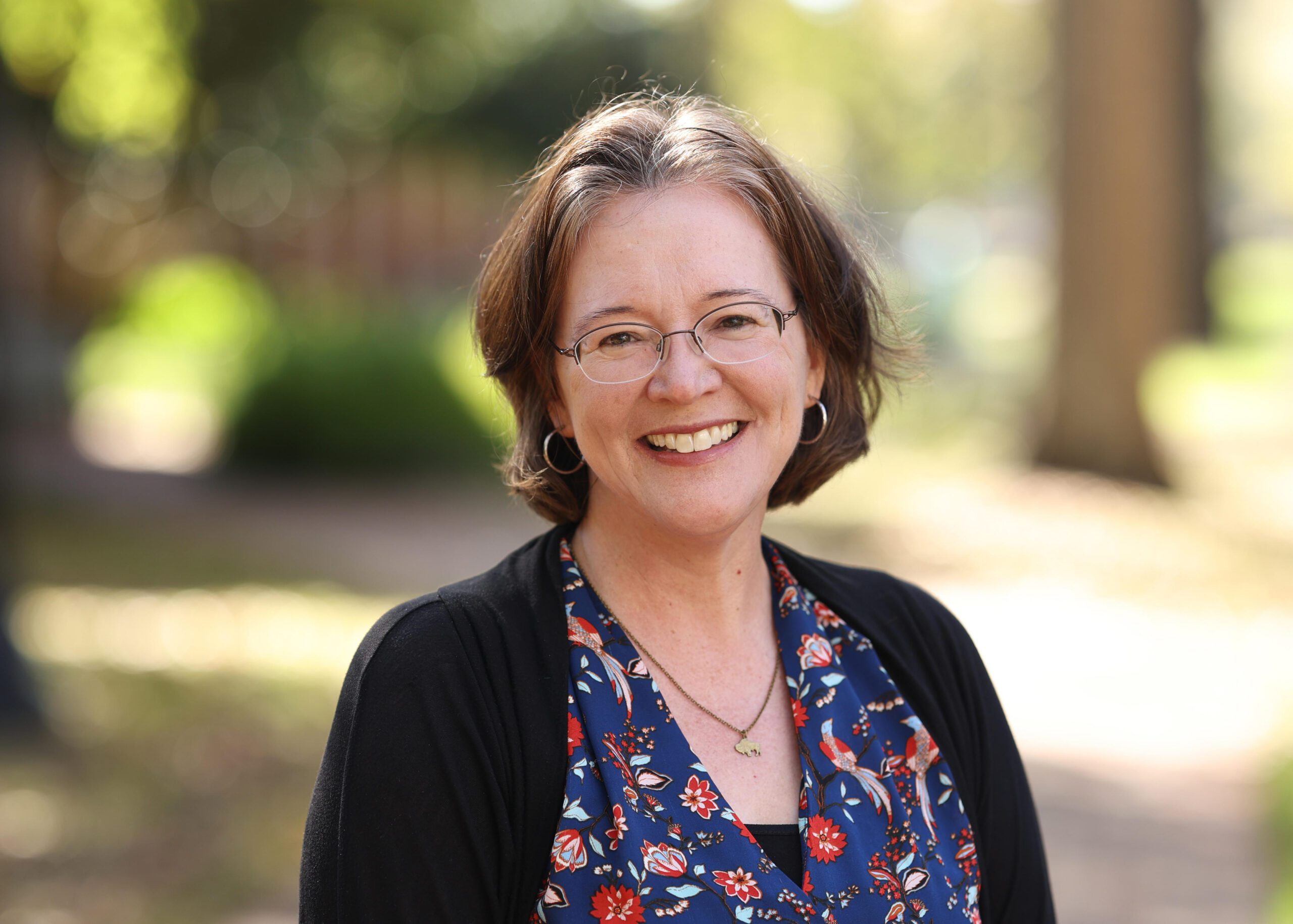 A woman wearing a blue shirt and glasses smiling outdoors