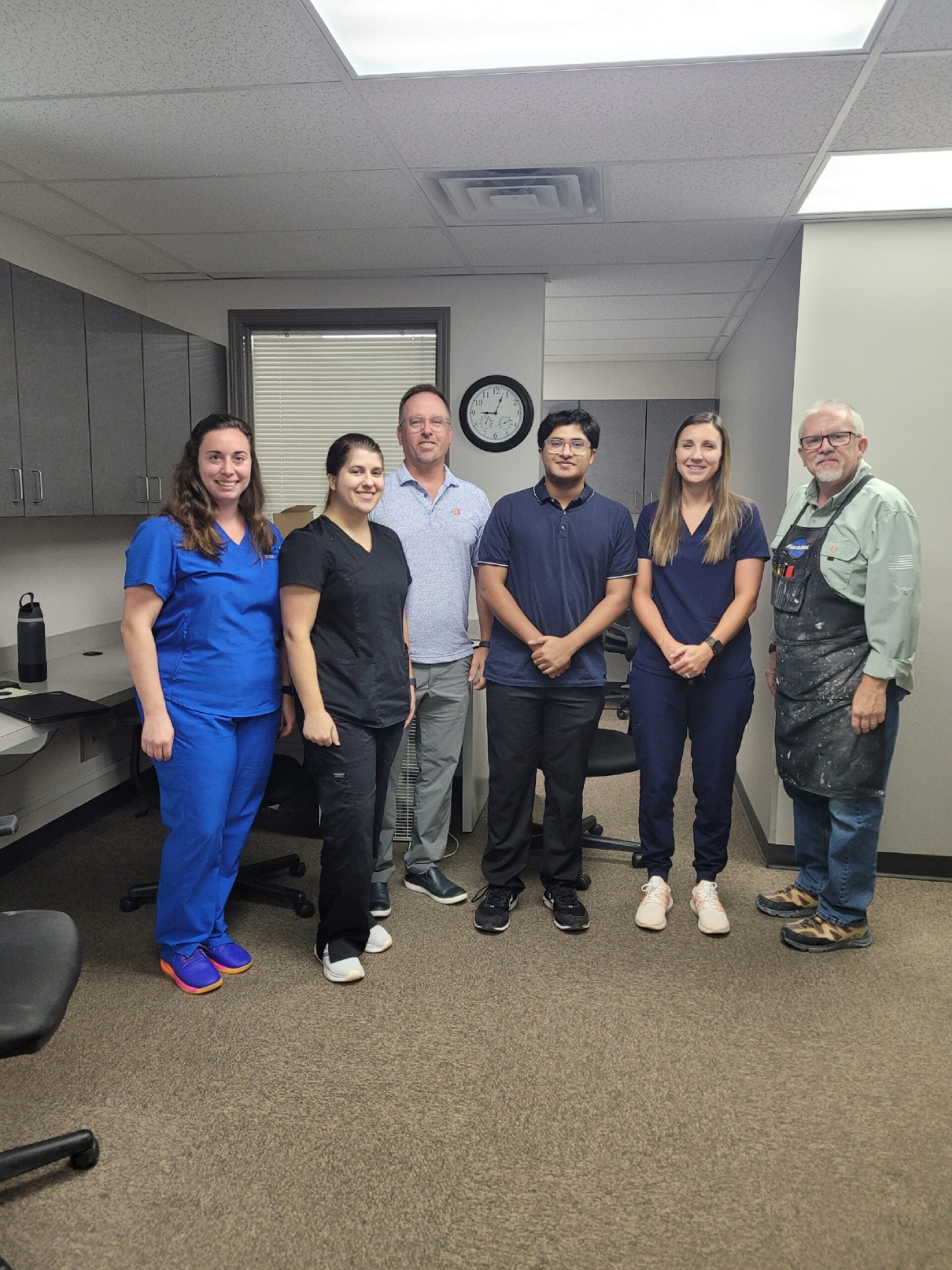 A group of six people stand together for a photo in an office