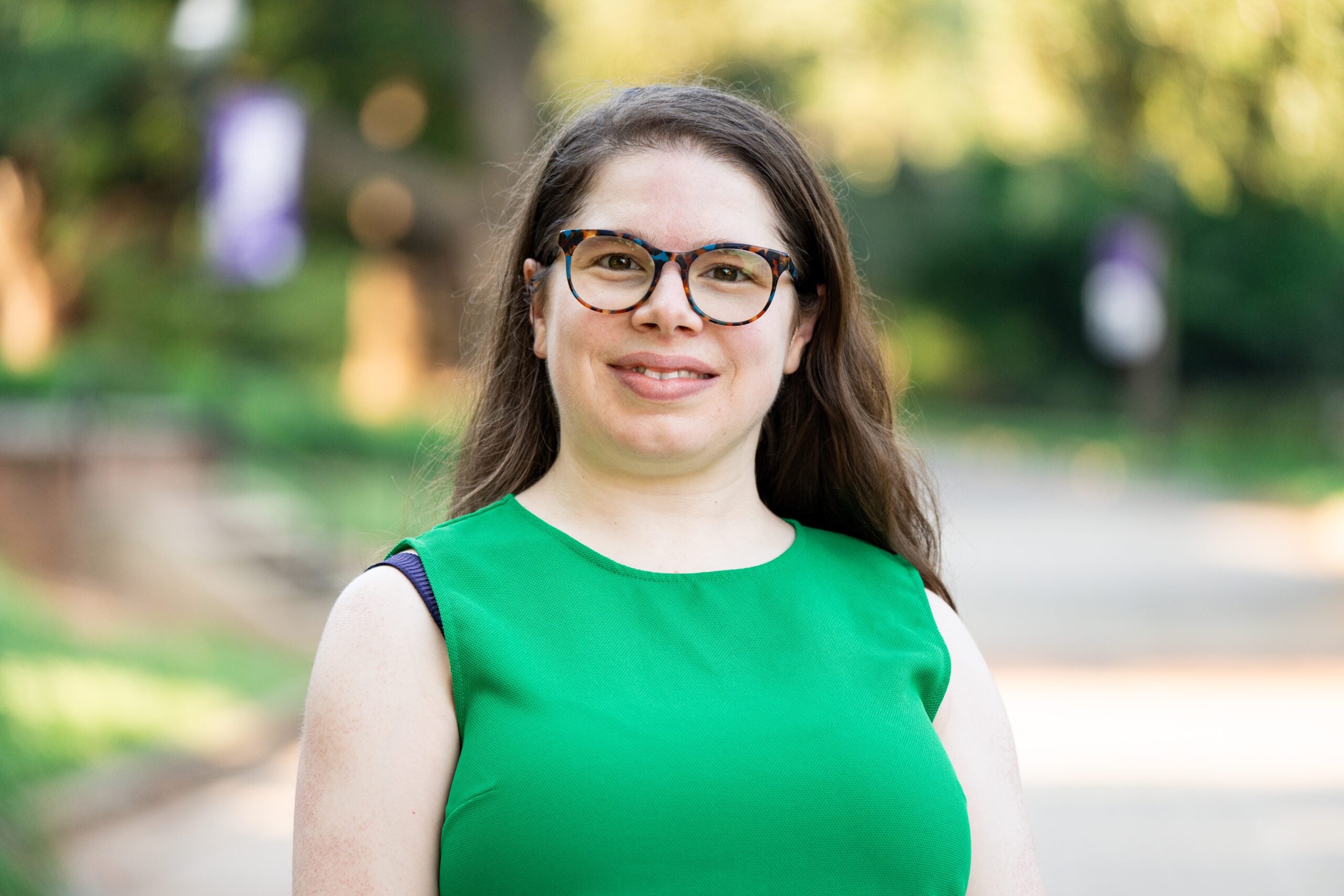 A photo of a woman with long brown hair, glasses, and a green top